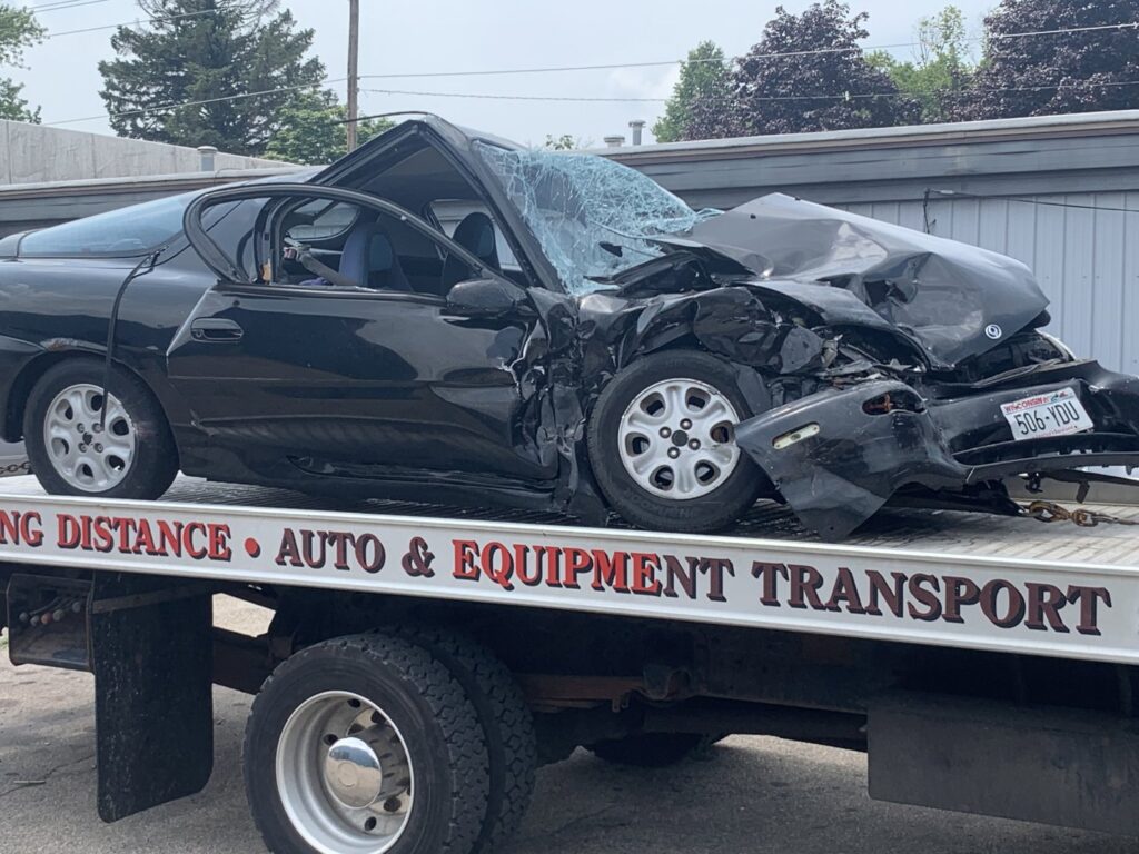 A&W Towing and Repair flatbed tow truck transporting a heavily damaged black car in Appleton, WI.