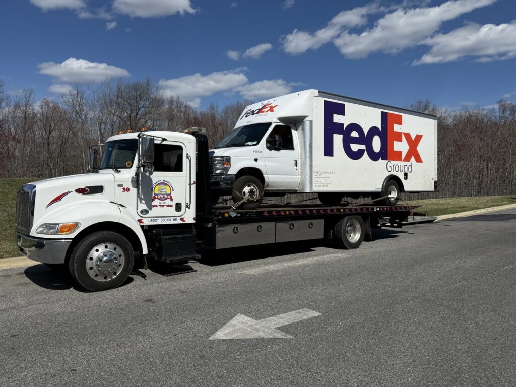 A flatbed tow truck transporting a FedEx delivery van for Southern Maryland Towing in Prince Frederick, MD.