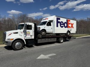 A flatbed tow truck transporting a FedEx delivery van for Southern Maryland Towing in Prince Frederick, MD.