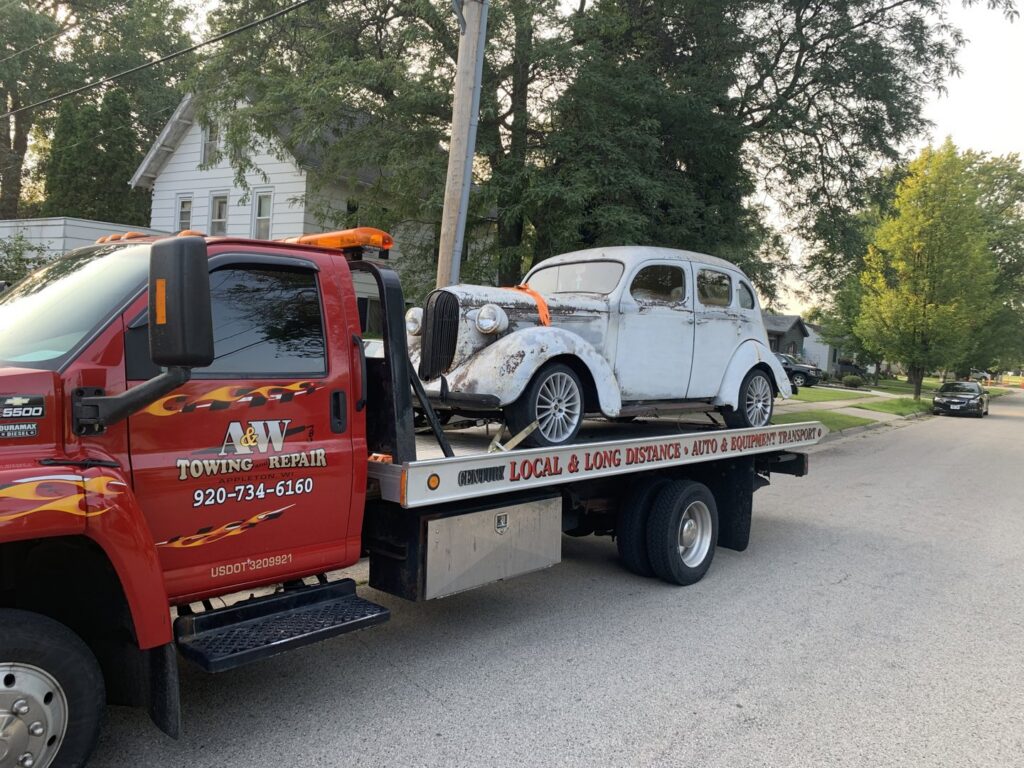 A&W Towing and Repair flatbed tow truck transporting an old white car in Appleton, WI.