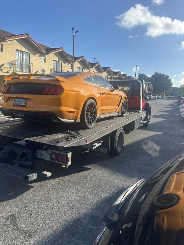 A flatbed tow truck from Rodicio Towing Services transporting an orange Ford Mustang in Hialeah, FL.