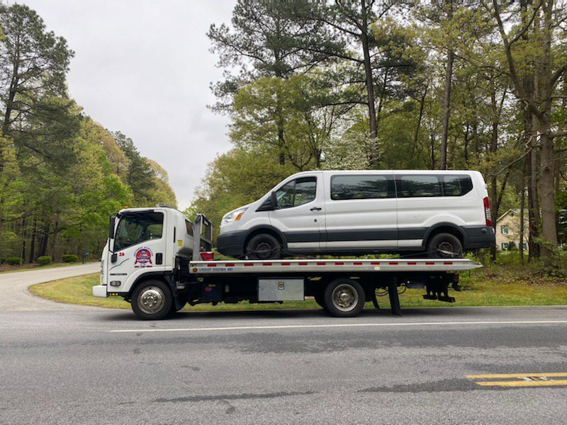 A flatbed tow truck transporting a white passenger van for Southern Maryland Towing in Prince Frederick, MD.