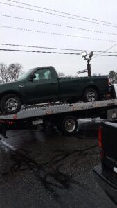 A flatbed tow truck transporting a green pickup truck in snowy conditions for Southern Maryland Towing in Prince Frederick, MD.