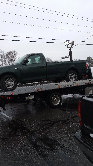 A flatbed tow truck transporting a green pickup truck in snowy conditions for Southern Maryland Towing in Prince Frederick, MD.