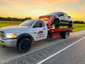 JM Towing & Transport LLC flatbed truck towing a pickup truck at sunset in Houston, TX.