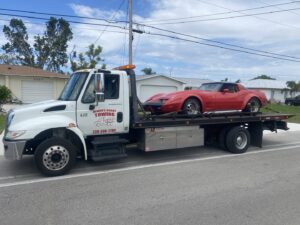 A flatbed tow truck from Always Ready Towing transporting a red classic car in North Fort Myers, FL.