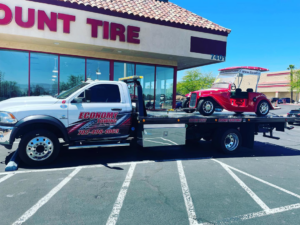 A white flatbed tow truck from Economy Towing transporting a red vintage-style golf cart in Las Vegas, NV.