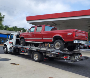 A white flatbed tow truck from Hank's Auto Service transporting a red pickup truck in Bethlehem, PA.