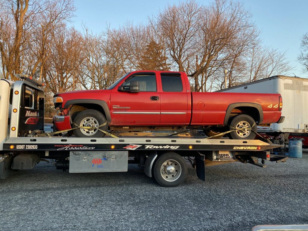 A white flatbed tow truck from Hank's Auto Service transporting a red pickup truck in Bethlehem, PA.