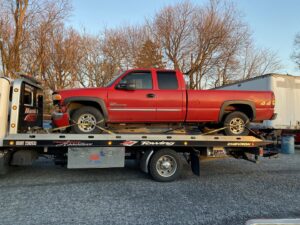 A white flatbed tow truck from Hank's Auto Service transporting a red pickup truck in Bethlehem, PA.
