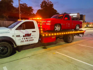 JM Towing & Transport LLC flatbed truck towing a red pickup truck in Houston, TX.
