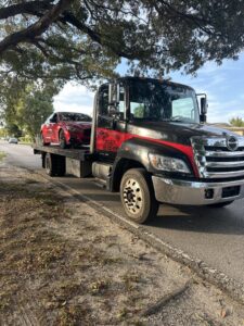A flatbed tow truck from Rodicio Towing Services transporting a red sedan in Hialeah, FL.