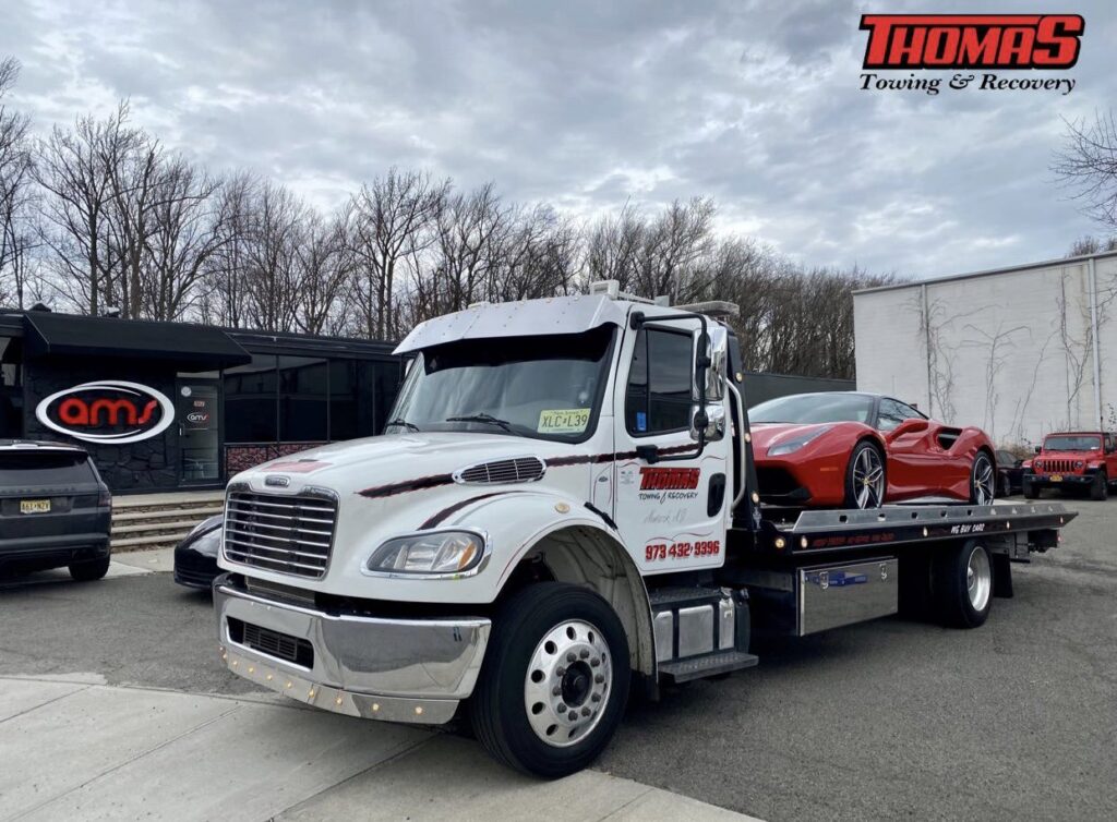 Thomas Towing & Recovery flatbed truck towing a red sports car in Newark, NJ.