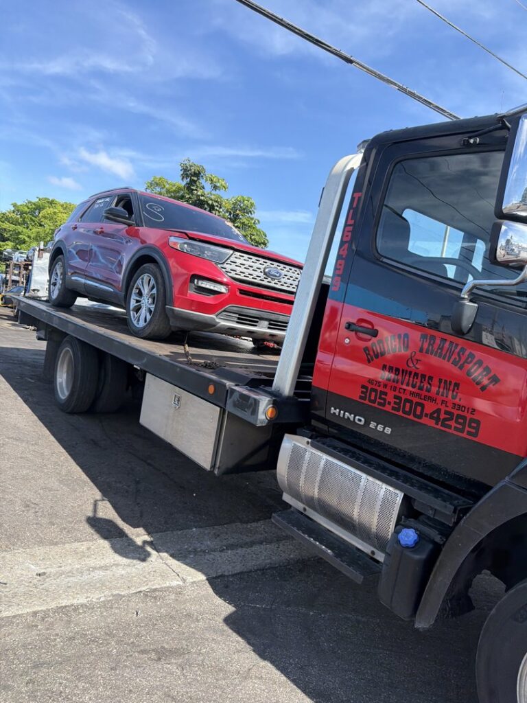 A flatbed tow truck from Rodicio Towing Services transporting a red SUV in Hialeah, FL.