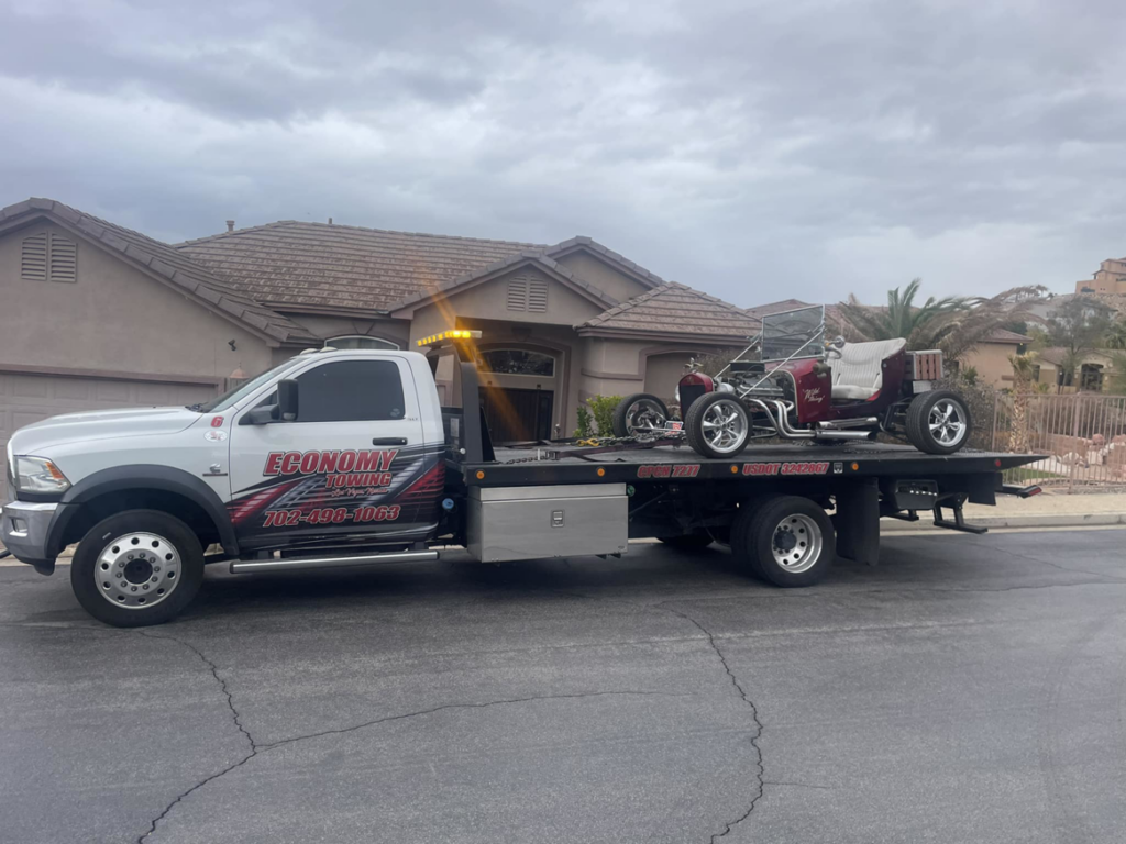 A white flatbed tow truck from Economy Towing transporting a red vintage hot rod in Las Vegas, NV.