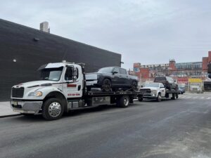 Thomas Towing & Recovery flatbed truck towing a grey Rivian pickup and another truck in Newark, NJ.
