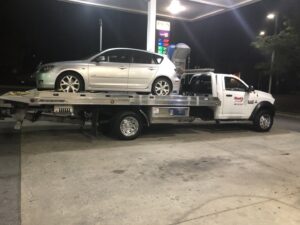 A white flatbed tow truck from Hank's Auto Service transporting a silver hatchback at night in Bethlehem, PA.