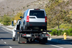A flatbed tow truck transporting a silver SUV for AE Recovery and Towing in Phoenix, AZ.