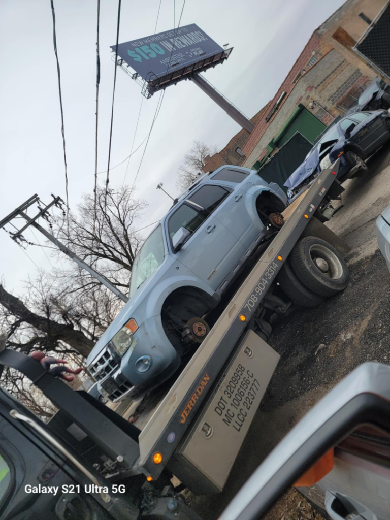 A flatbed tow truck from Soto Towing Inc. towing a light blue SUV with missing wheels in Chicago, IL.