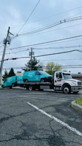 Thomas Towing & Recovery flatbed truck towing two light blue vans in Newark, NJ.