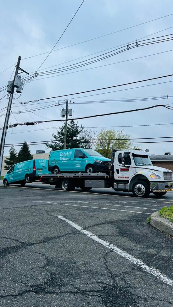 Thomas Towing & Recovery flatbed truck towing two light blue vans in Newark, NJ.