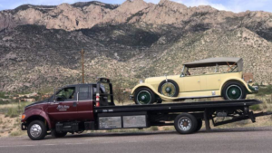 A flatbed tow truck from All Pro Towing & Recovery, Inc. towing a vintage yellow car with mountains in Albuquerque, NM.
