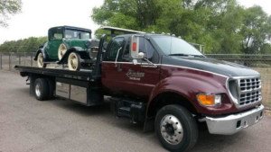 A flatbed tow truck from All Pro Towing & Recovery, Inc. towing a vintage green car in Albuquerque, NM.