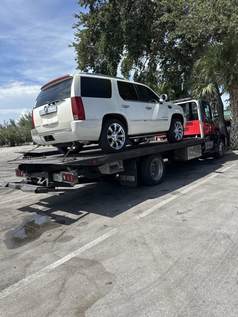 A flatbed tow truck from Rodicio Towing Services transporting a white Cadillac Escalade in Hialeah, FL.