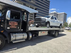 A flatbed tow truck from Allan Motors & Wrecker Service LLC towing a white pickup truck in Houston, TX