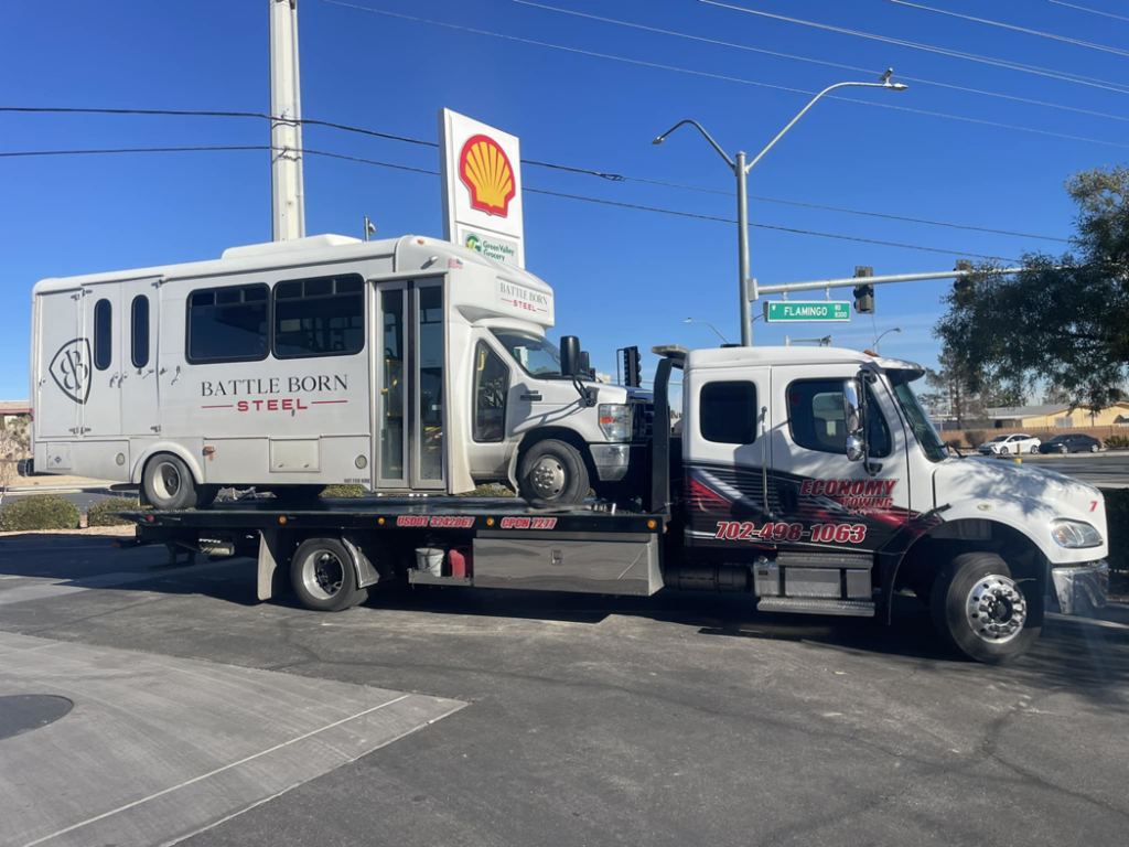 Economy Towing's flatbed truck transporting a white shuttle bus on a sunny day in Las Vegas, NV.