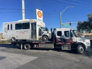 Economy Towing's flatbed truck transporting a white shuttle bus on a sunny day in Las Vegas, NV.