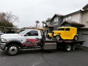 A white flatbed tow truck from Economy Towing transporting a yellow vintage car in Las Vegas, NV.