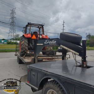 A flatbed trailer from Sunny Acres Towing transporting an orange tractor in Greenville, IN.