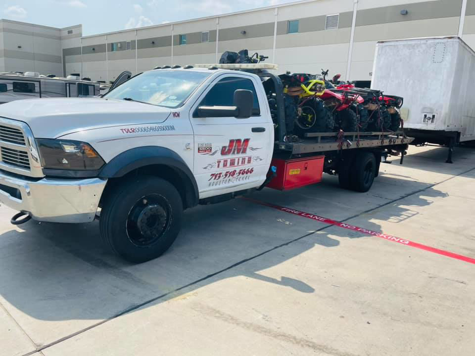 JM Towing & Transport LLC flatbed truck transporting ATVs and a trailer in Houston, TX.