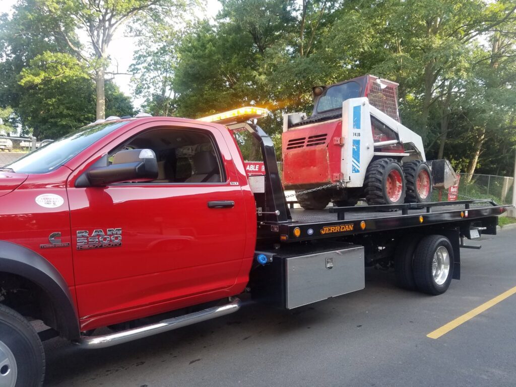 A Velez Towing flatbed truck transporting a red and white bobcat loader in Newark, NJ.
