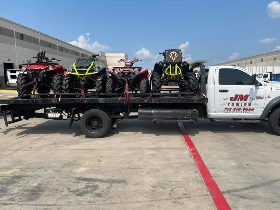 JM Towing & Transport LLC flatbed truck transporting four ATVs in Houston, TX.