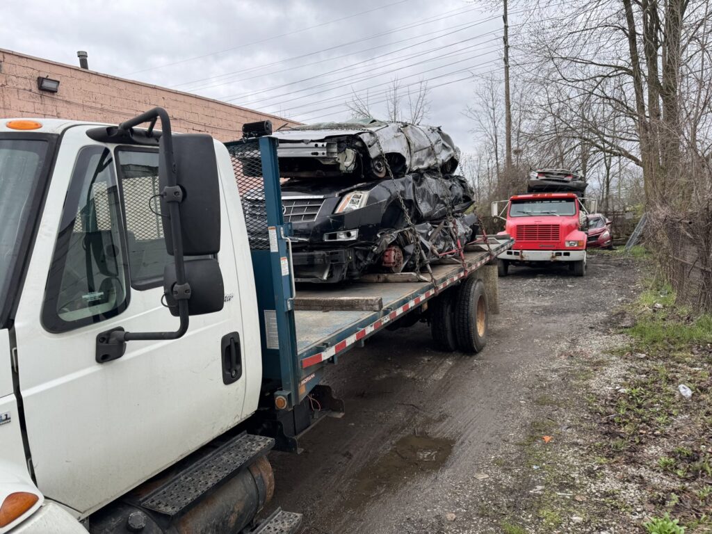 A flatbed truck from ALDM Management loaded with multiple severely damaged junk cars for removal in Cleveland, OH.