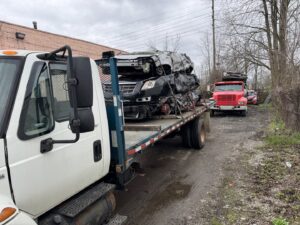 A flatbed truck from ALDM Management loaded with multiple severely damaged junk cars for removal in Cleveland, OH.