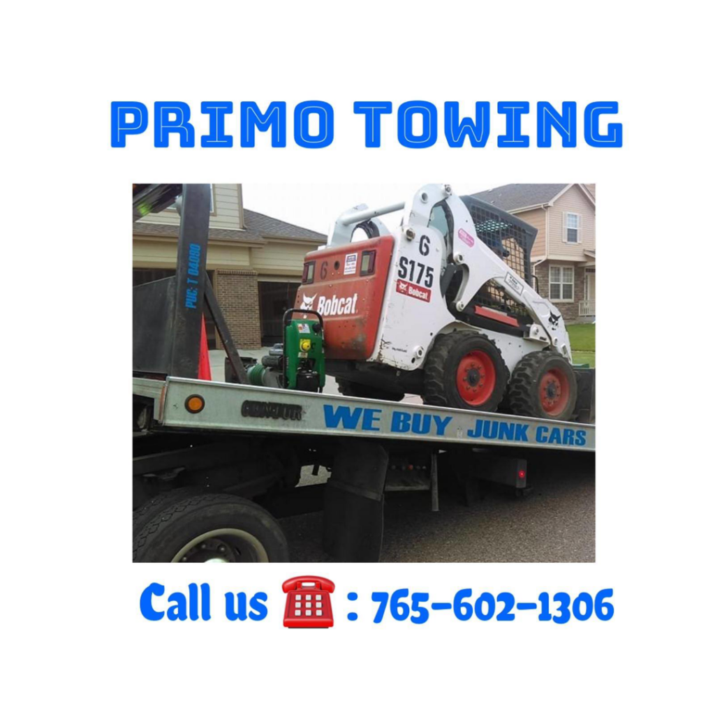 A Primo Towing flatbed truck transporting a Bobcat skid-steer loader in Anderson, IN.