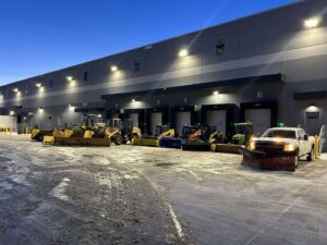 A fleet of snow removal vehicles, including plows and loaders, parked at a commercial site by Turf Pro Lawn Care & Snow Removal in Green Bay, WI.