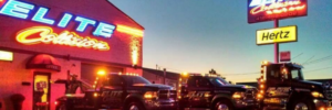 A fleet of Elite Collision tow trucks parked outside the business at night, offering towing services in Pittsburgh, PA.