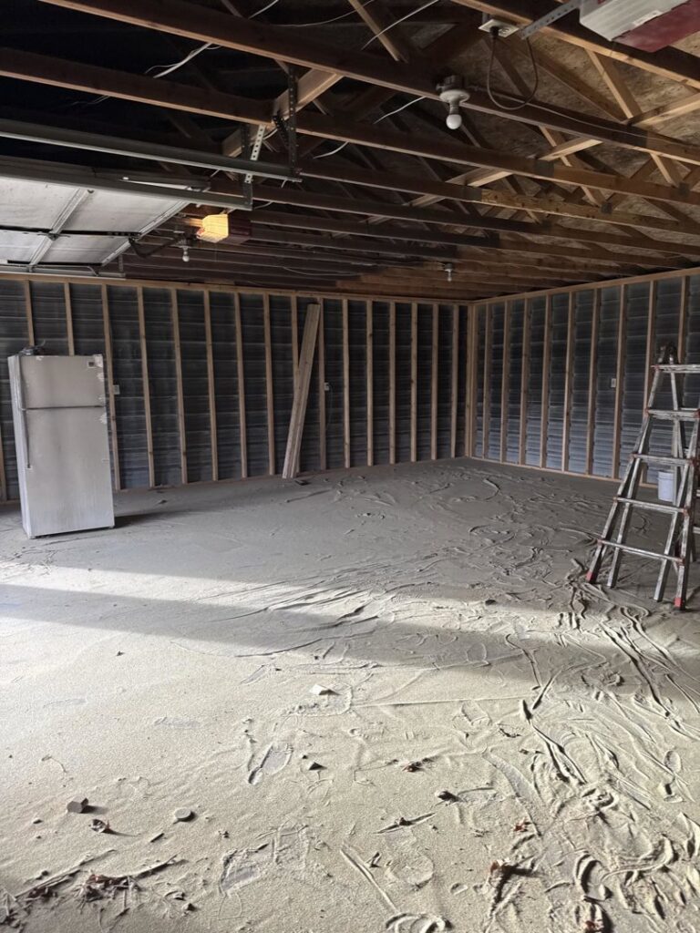 A garage floor covered in sand and debris from flood cleanup by 406 Disaster Response in Billings, MT.
