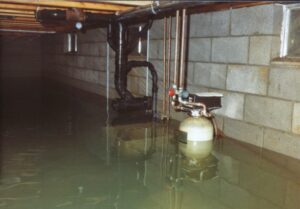 A flooded basement or crawl space with a large amount of standing water submerging pipes and equipment, showing severe water damage in Oakland, CA by One Call Services of Oakland.