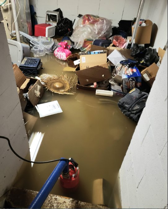 A severely flooded basement with debris and a water pump in action, handled by SO-CO Water Damage in Pueblo, CO.