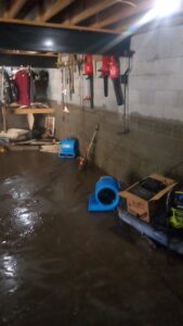 A flooded basement with standing water and industrial air movers for drying by Elements of Restoration in Denver, CO.