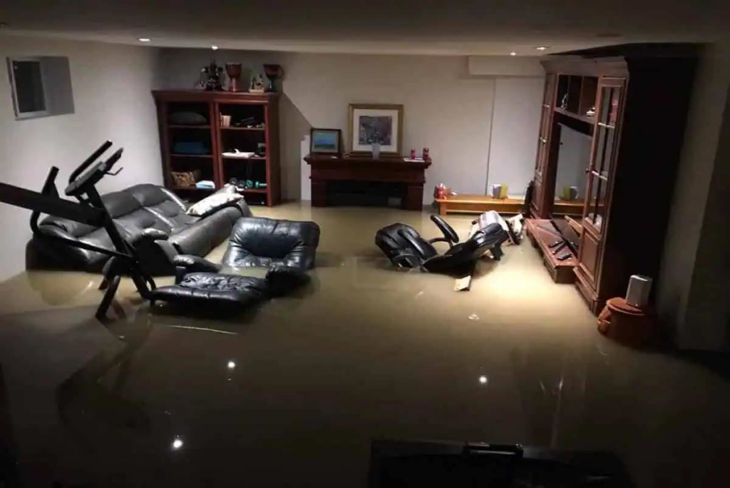 A severely flooded basement with furniture submerged in dirty water, indicating a major water damage issue for Ciocca Cleaning & Restoration in Fort Wayne, IN.