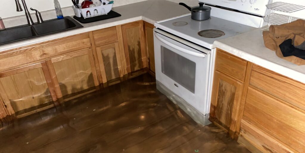 A kitchen floor covered in standing water and water-damaged cabinets, requiring restoration by Flow State Restoration in Gilbert, AZ