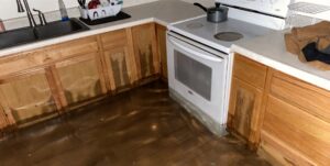 A kitchen floor covered in standing water and water-damaged cabinets, requiring restoration by Flow State Restoration in Gilbert, AZ