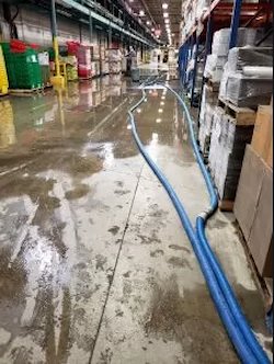 A flooded warehouse aisle with standing water and hoses for water removal by Restoration 1 of OKC in Yukon, OK.