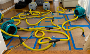 Specialized floor drying equipment with air movers and hoses on hardwood floor for water damage restoration by Lowcountry Remediation in Charleston, SC.